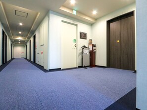 Un pasillo largo y estrecho con piso alfombrado, paredes blancas y una puerta de madera al final.