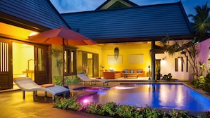 A poolside area with lounge chairs, a red umbrella, and a well-lit interior.
