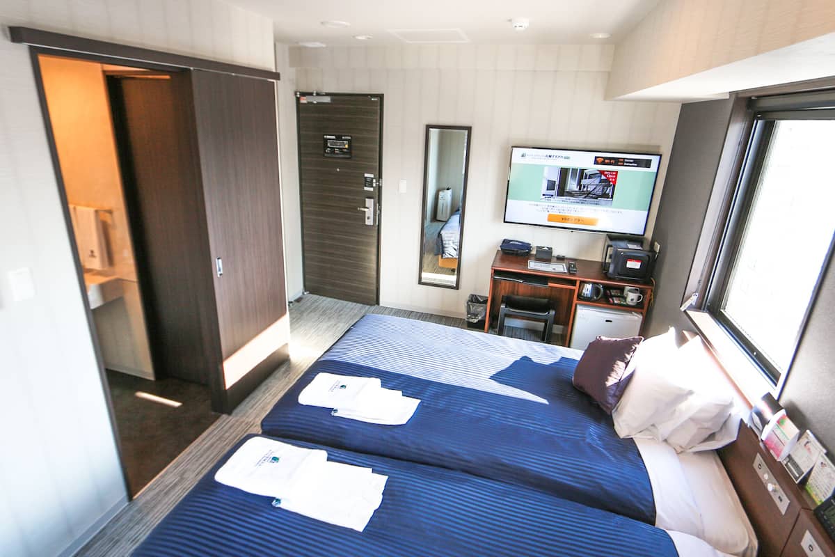 A hotel room with two beds, a desk, a television, and a mirror.