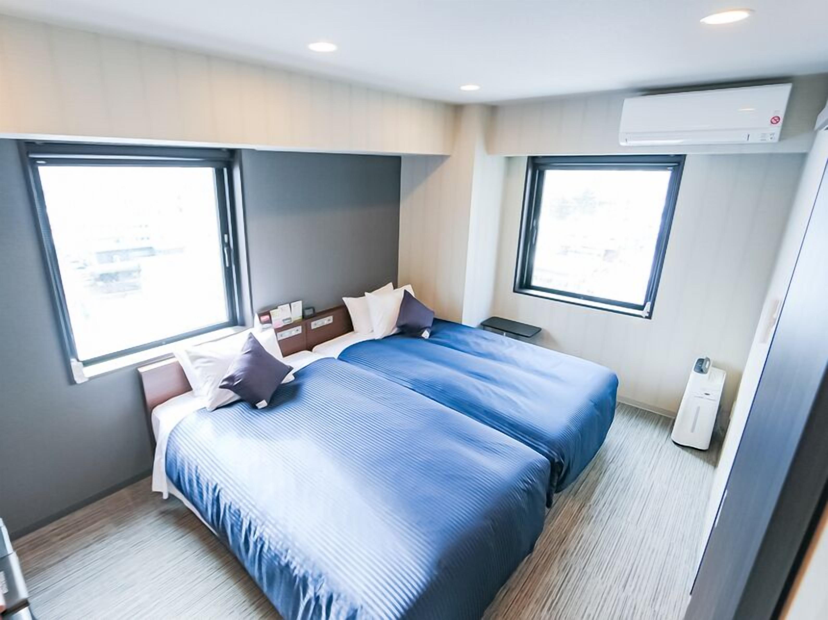 A hotel room with two beds, a window, and an air conditioning unit.