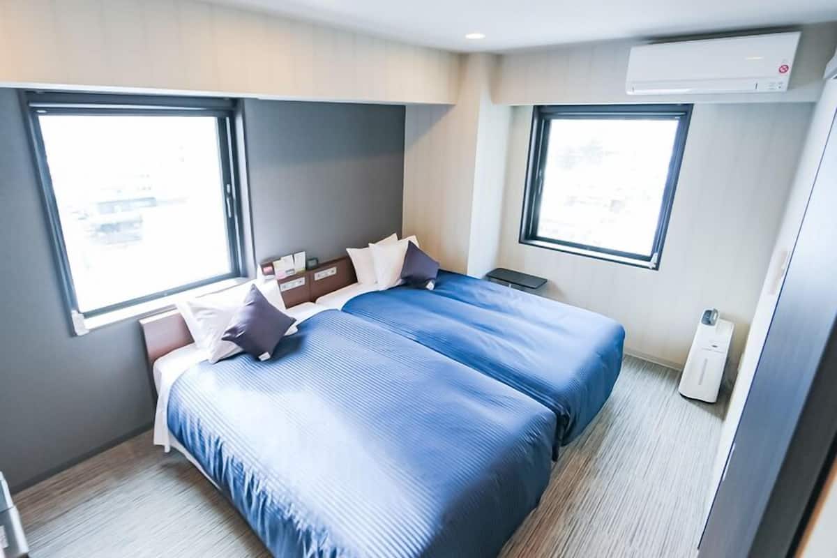 A hotel room with two beds, a window, and an air conditioning unit.