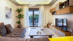 A modern living room with a sofa, a coffee table, a TV, and a potted plant. - Anesis Villa, with Private Pool & BBQ, Walking distance to the beach & amenities (Rethymno)