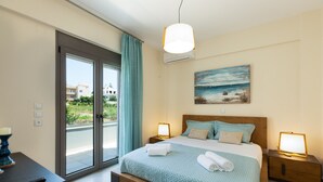 A bedroom with a large bed, two bedside tables with lamps, a painting on the wall, and a view through the sliding glass door. - Anesis Villa, with Private Pool & BBQ, Walking distance to the beach & amenities (Rethymno)