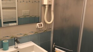 Een badkamer met een witte wastafel, een spiegel, een handdoekhouder met een gele handdoek, een douche met een glazen deur en een wandradiator.