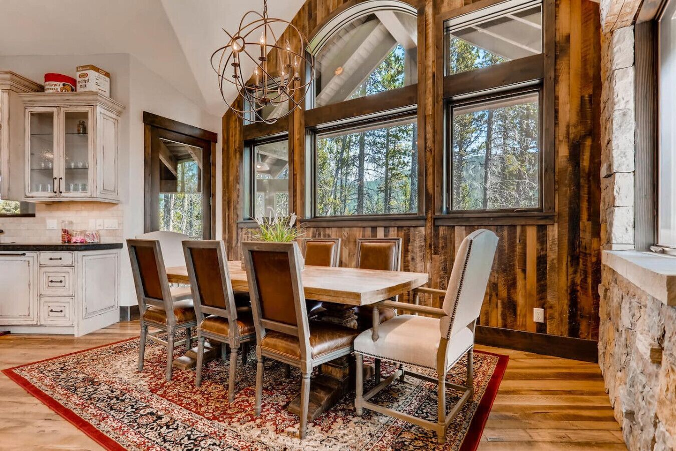 Un coin repas avec une table et des chaises en bois, de grandes fenêtres et une vue sur la forêt.
