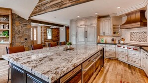 A spacious kitchen with a large marble island, wooden beams, and white cabinetry.