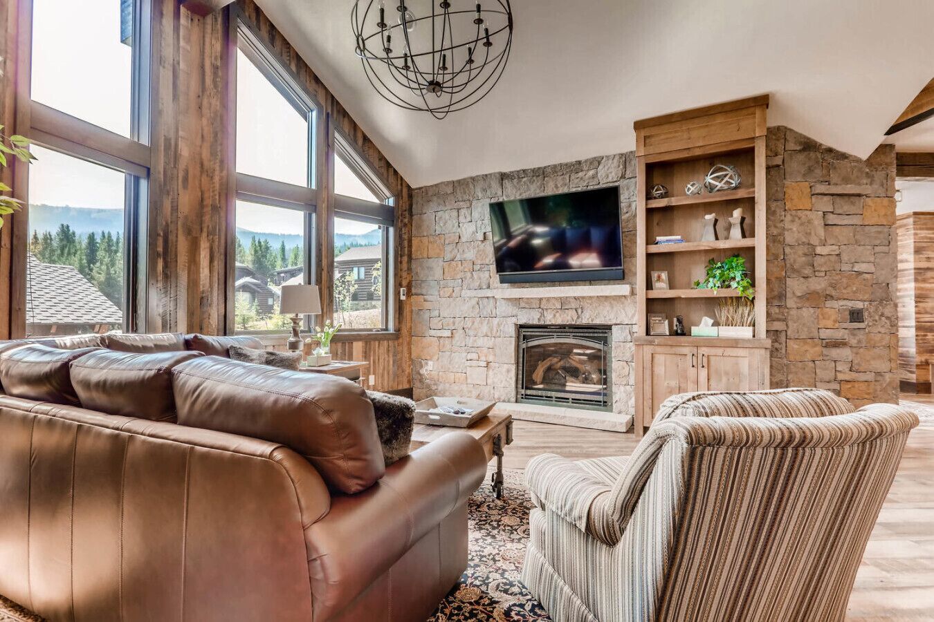 Ein geräumiges Wohnzimmer mit Kamin aus Stein, einer Ledersofa und einem an der Wand montierten Fernseher.