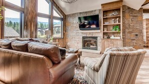 A spacious living room with a stone fireplace, leather sofa, and a television mounted on the wall.