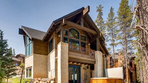 A two-story log cabin with a stone foundation, a balcony, and a hot tub in the foreground.