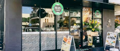 A modern building with a MAX CAFE sign, a visible entrance, and a signboard for lunch.