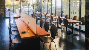 Een modern café interieur met houten tafels en zwarte stoelen, grote ramen met uitzicht op de straat, en een strak, minimalistisch design.