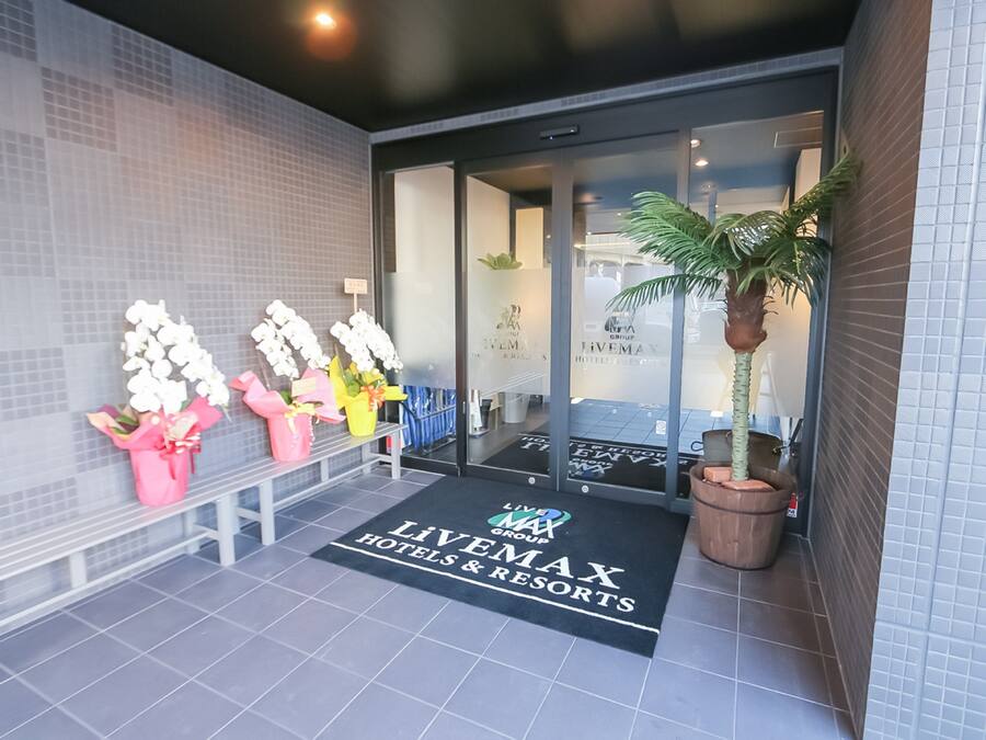 A hotel entrance with a reception desk, potted plants, and a welcome mat.