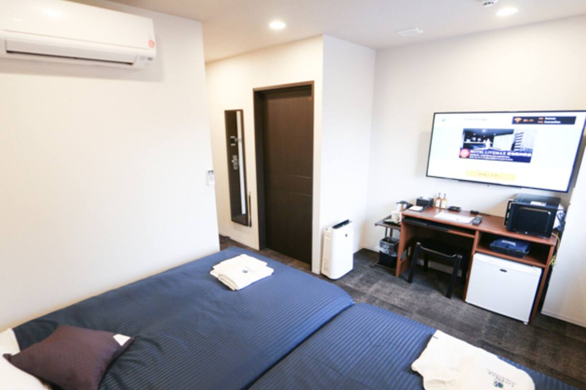 A hotel room with a bed, a desk, a small refrigerator, and a wall-mounted TV.