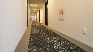Een hotelgang met een kamerbreed tapijt, een brandmelder aan de muur en een plafond met inbouwspots.