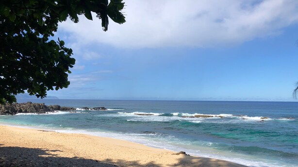 Una platja amb aigua blava i cristal·lina, sorra daurada i roques a la vora.
