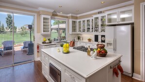 A spacious kitchen with white cabinetry, a large island, and a view of a patio with outdoor furniture. - Stunning golf course view vacation home (Tustin)