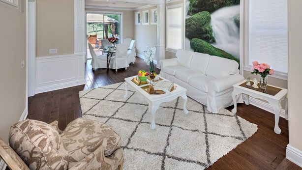 A spacious living room with a white sofa, a coffee table with decorative items, and a large window with a view of a green landscape. - Stunning golf course view vacation home (Tustin)