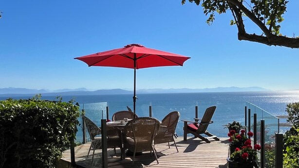 A wooden deck with wicker chairs and a red umbrella, overlooking a scenic view of the sea and mountains. -  Secluded Sandy Beach All To Yourself! Panoramic Ocean and Mountain views. (Comox)