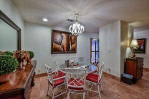 Uma sala de jantar com uma mesa redonda, cadeiras brancas com almofadas vermelhas, um candelabro e um quadro de um elefante na parede.