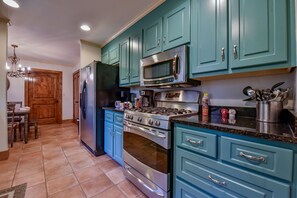 Una cocina con gabinetes color turquesa, electrodomésticos de acero inoxidable y piso de baldosas.