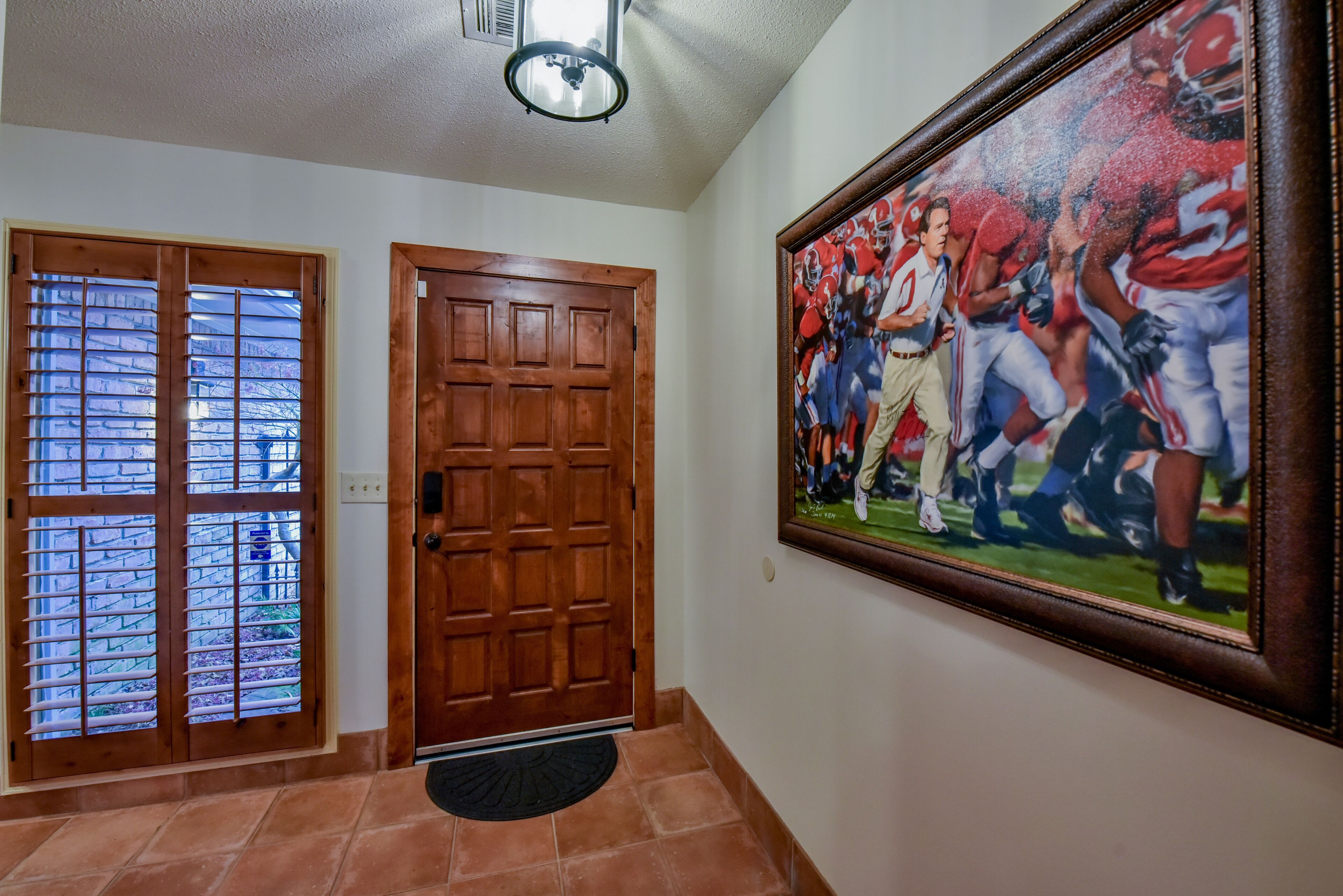 A hallway with a wooden door, a window with blinds, and a framed sports team photo on the wall.