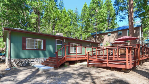 Une cabane à l’extérieur rouge, avec des fondations en pierre et une terrasse en bois dotée d’une rambarde en métal.