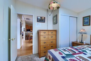 A bedroom with a wooden dresser, a bed with a quilt, a desk with a lamp, and a door leading to another room. - (42R) Rosenberg's Creekside Cabin at The Redwoods In Yosemite (Yosemite National Park)