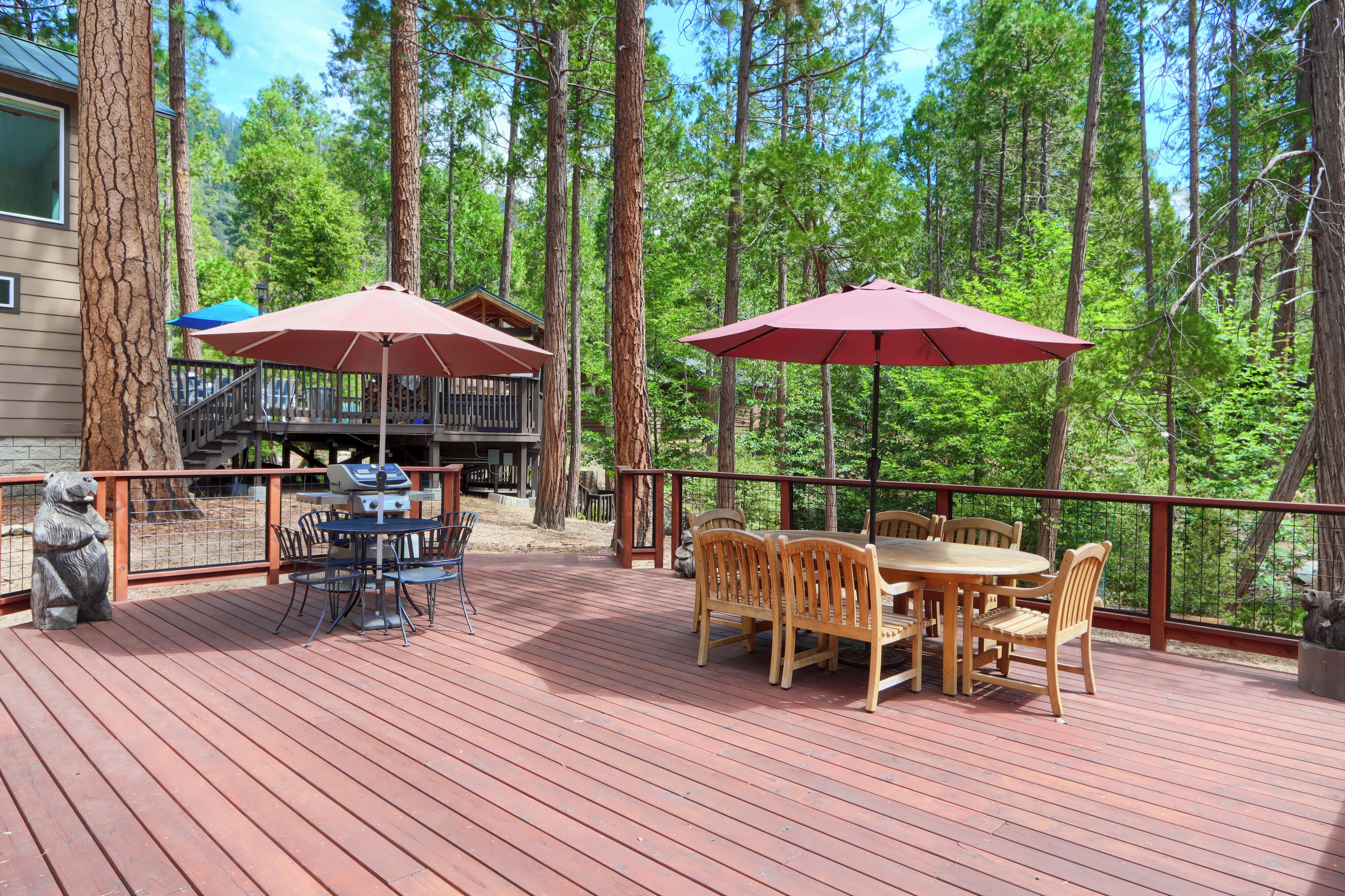 Une terrasse en bois, meublée pour l’extérieur, avec deux parasols et une vue sur une zone boisée.