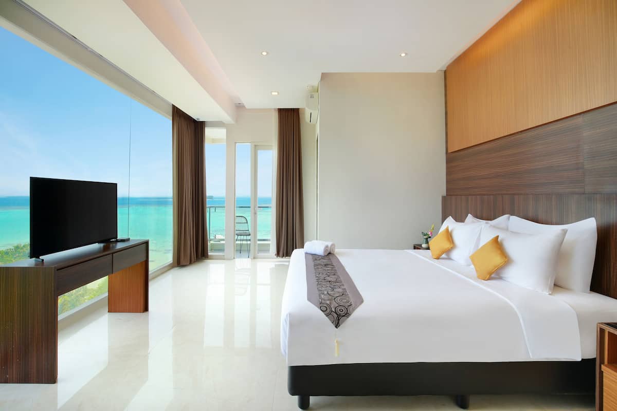 A modern hotel room with a large bed, a flat-screen TV, and a view of the ocean.