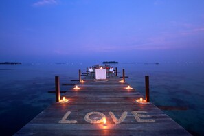 Une jetée en bois sur laquelle est inscrit le mot « AMOUR », menant à une table dressée pour deux, agrémentée de bougies.