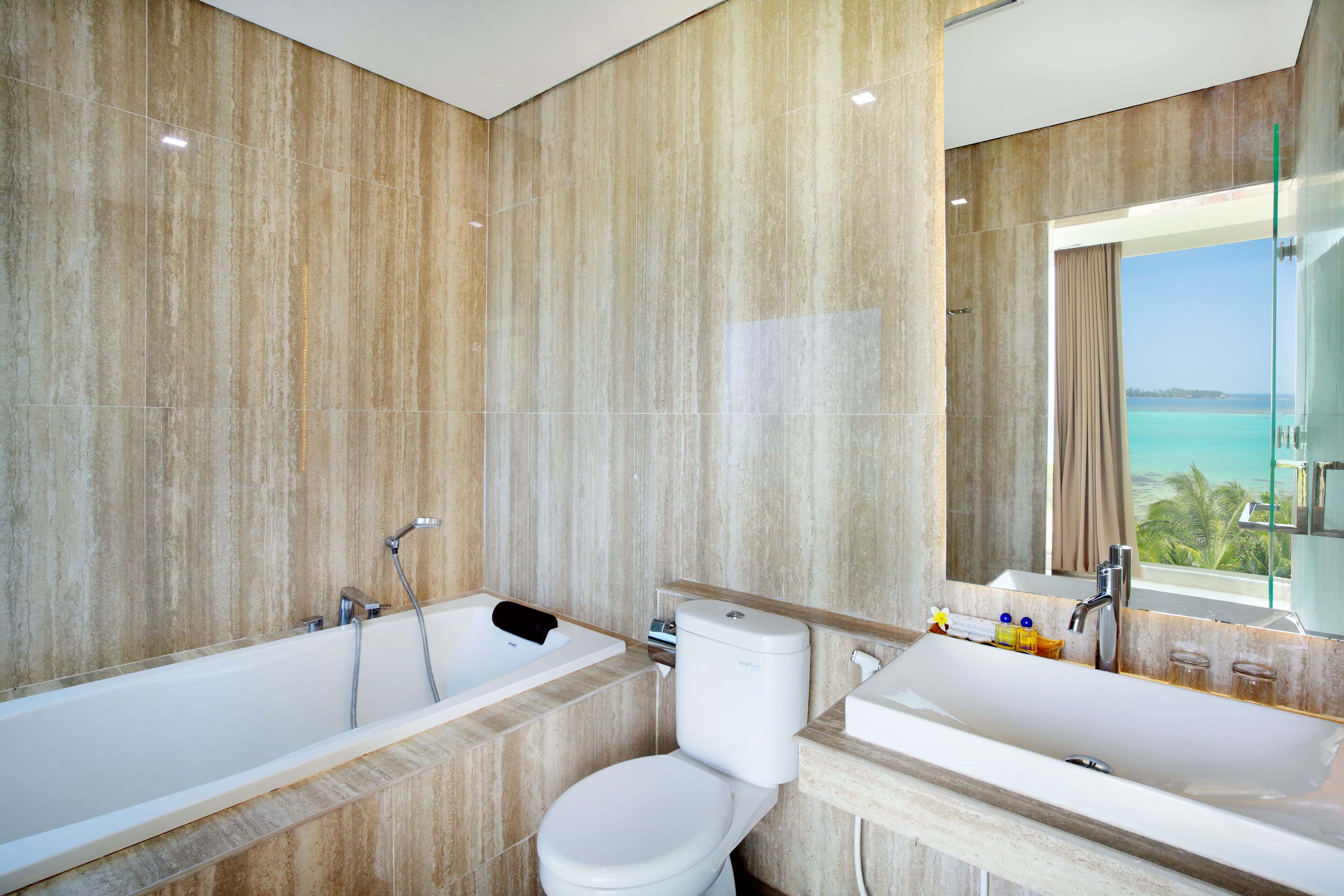 Ein modernes Badezimmer mit Badewanne, Toilette und Waschbecken, ausgestattet mit einem großen Spiegel und Meerblick.