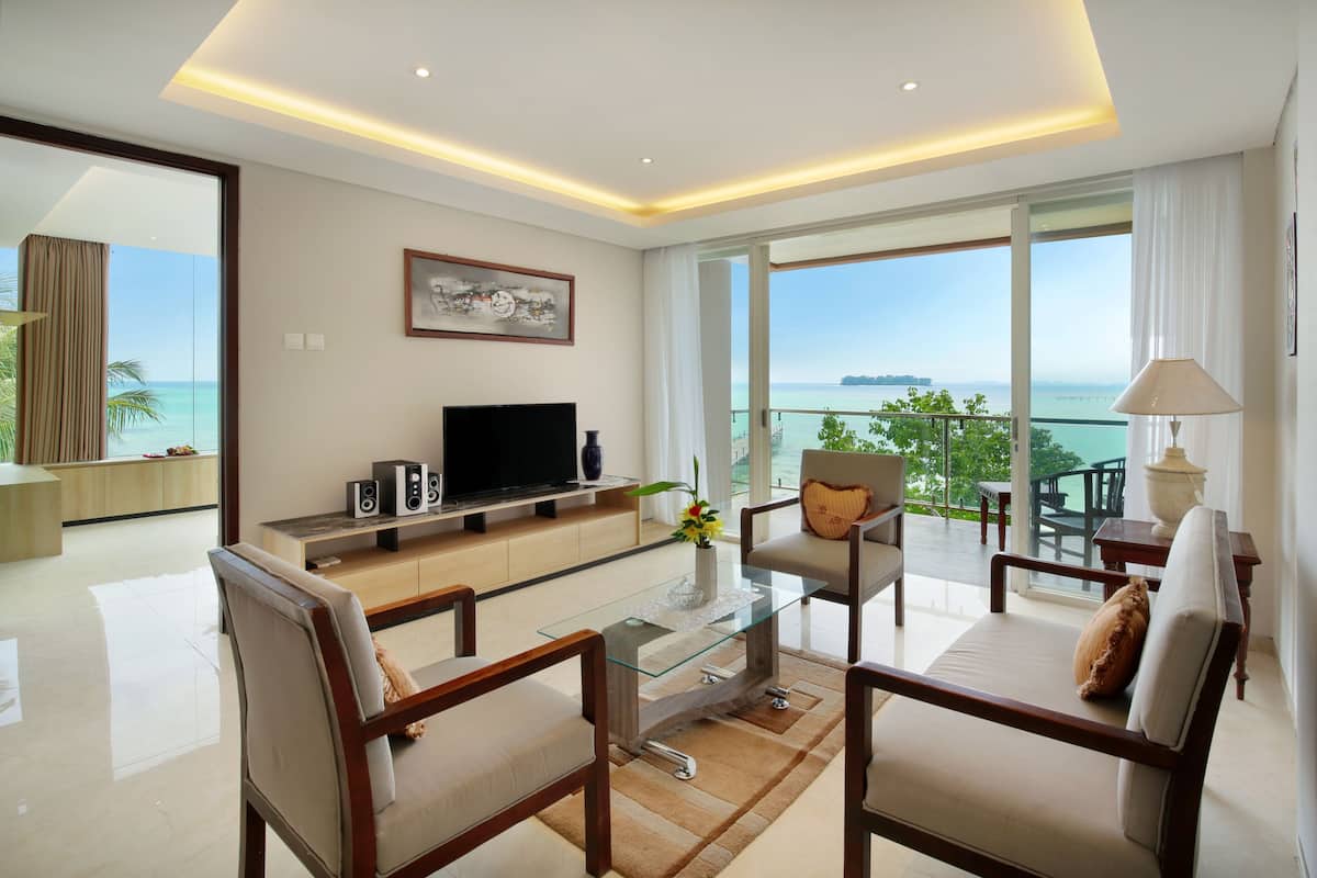 A modern living room with a glass coffee table, two armchairs, a sofa, a flat-screen TV, and a painting on the wall.