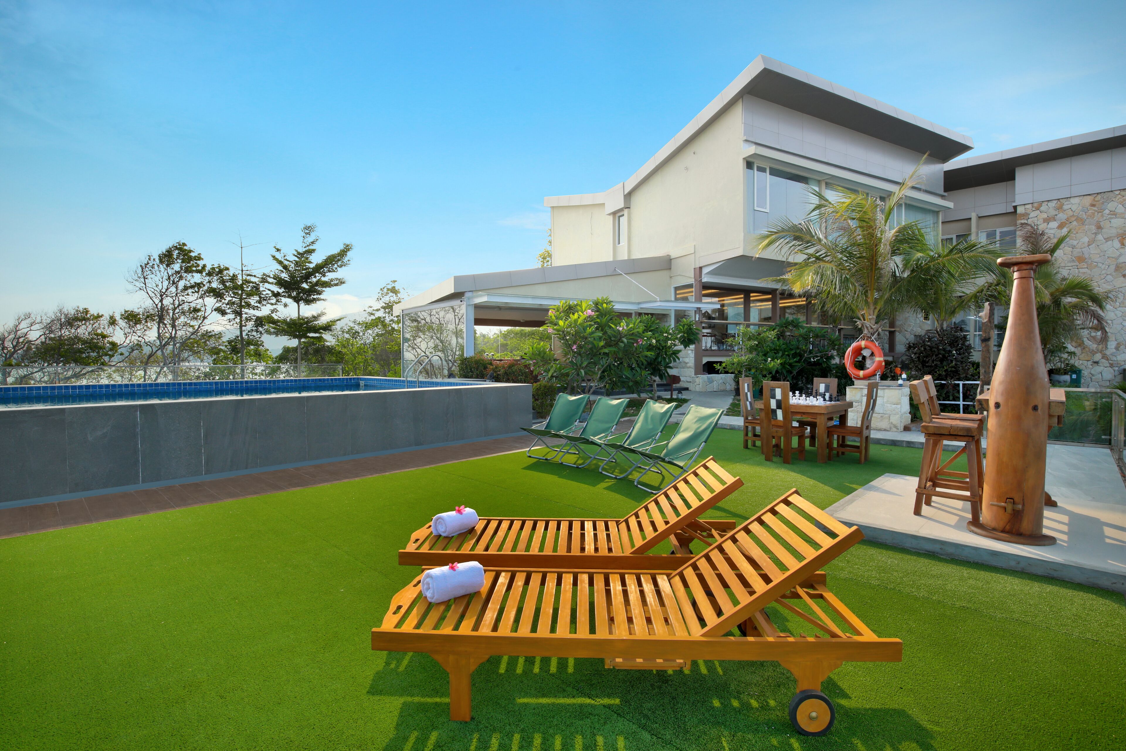 A rooftop terrace with artificial grass, sun loungers, and a large planter.