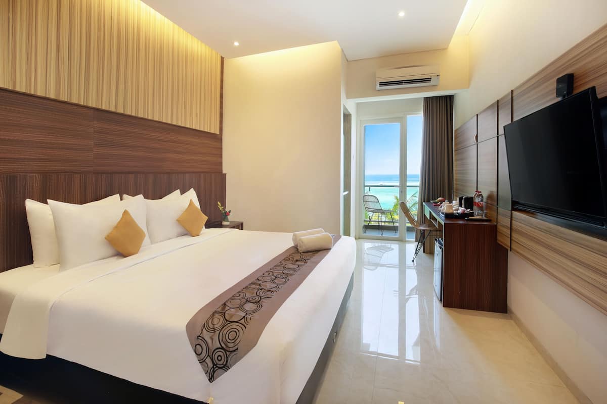 A hotel room with a large bed, a TV, a desk, and a view of the ocean.