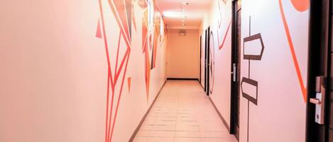 A hallway with a tiled floor, walls with geometric patterns, and doors with labels.