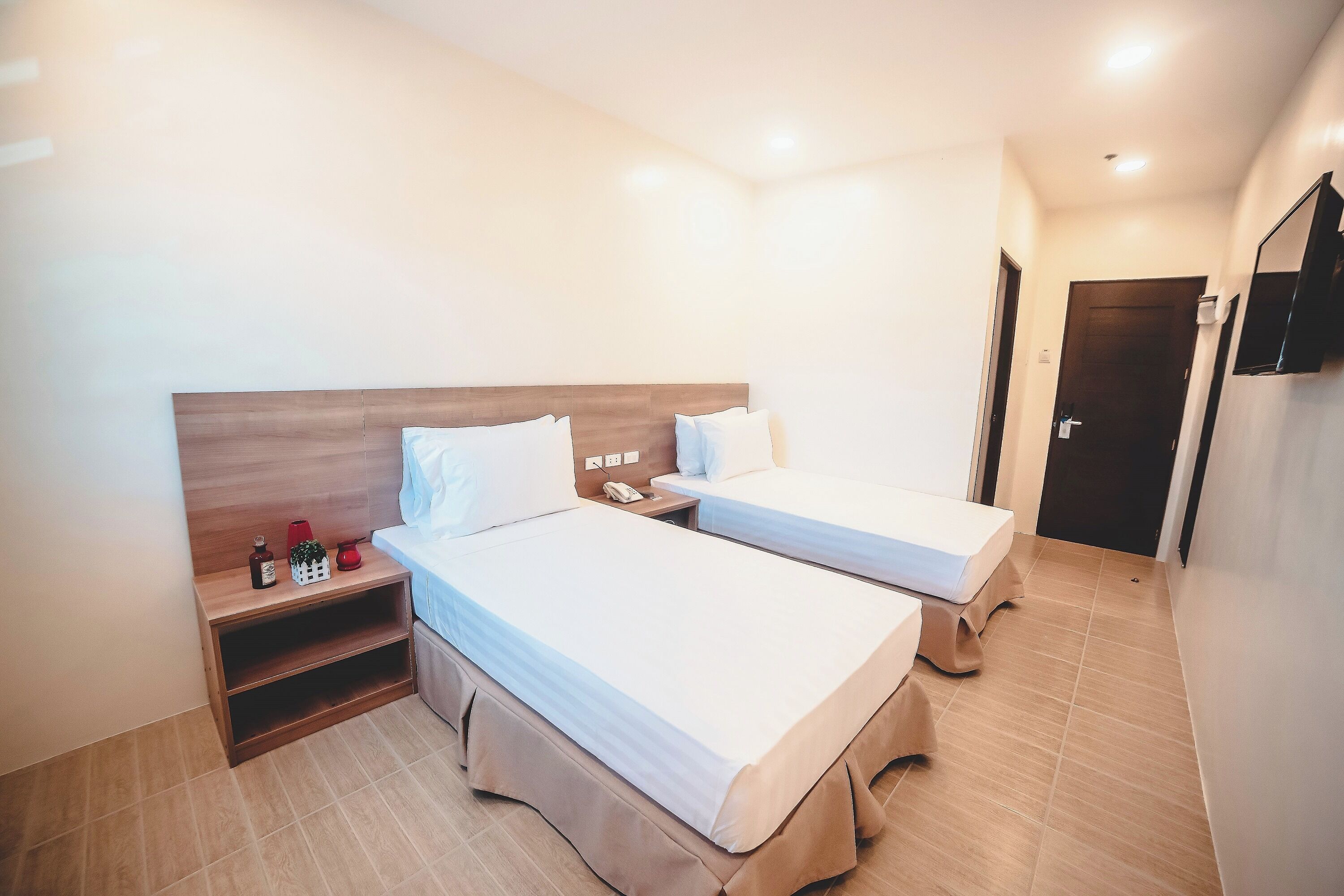 Une chambre d’hôtel avec deux lits, une tête de lit en bois, une table de chevet avec un téléphone et une petite étagère contenant des articles de toilette.