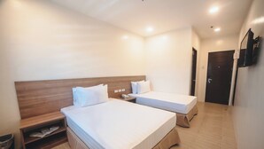 A hotel room with two beds, a wooden headboard, a small shelf, and a trash bin.