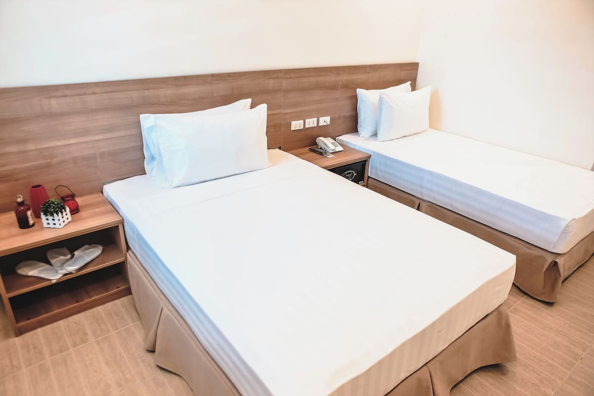 A hotel room with two beds, a wooden headboard, a bedside table with a phone, and a shoe rack.
