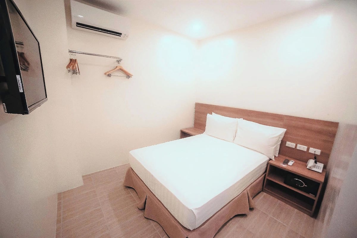 A hotel room with a bed, bedside table, and a mirror.