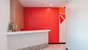 A reception area with a red wall, a white reception desk, and a patterned border at the base.