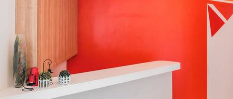 A reception desk with a white counter, a red wall, and a wooden panel to the left.