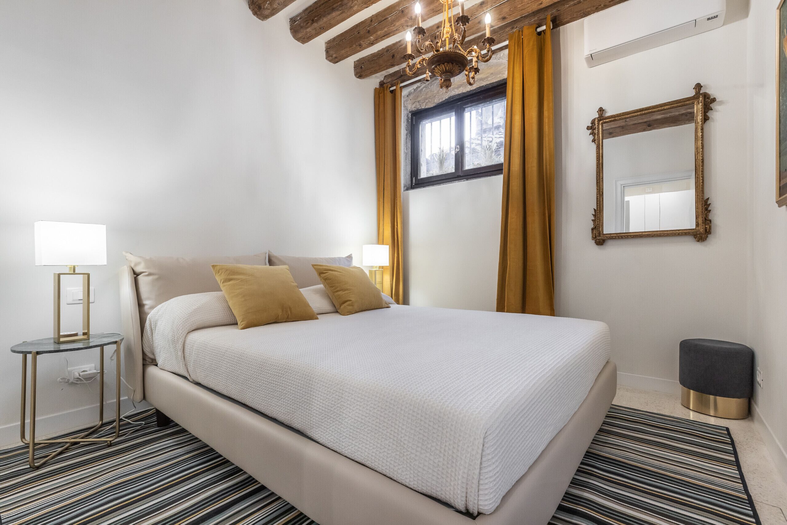Quarto bem organizado com cama, abajures, espelho e janela com cortinas.