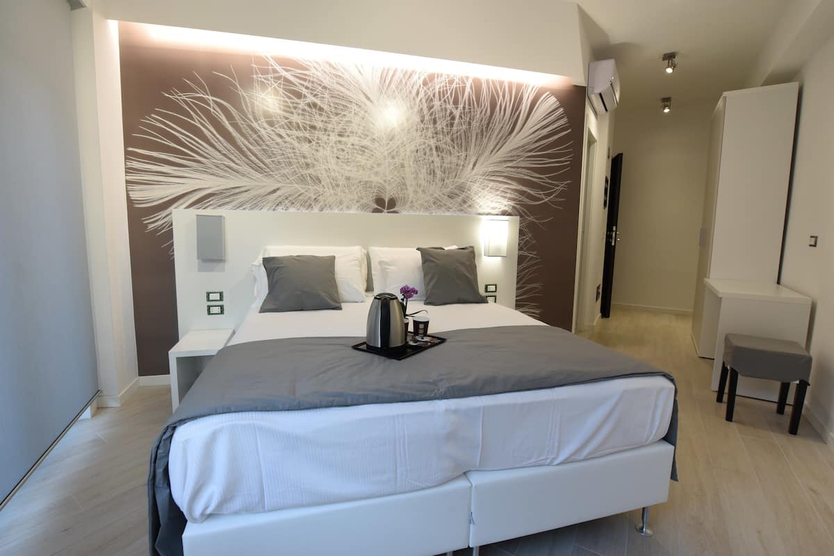 A modern bedroom with a large bed, a decorative wall, bedside tables, and a small seating area.