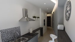 A modern kitchen with a stainless steel sink, a black countertop, a grey cabinet, a black and white tiled backsplash, a stainless steel range hood, and a white microwave on a dark countertop. - Duca's House (Rome)