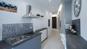 A modern kitchen with a black countertop, stainless steel sink, and a tiled backsplash. There is a large clock on the wall and a window with a view of the outside. - Duca's House (Rome)