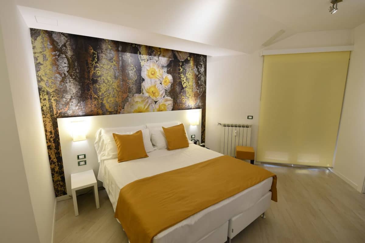A modern hotel room with a large bed, a nightstand, a wall-mounted lamp, and a radiator.