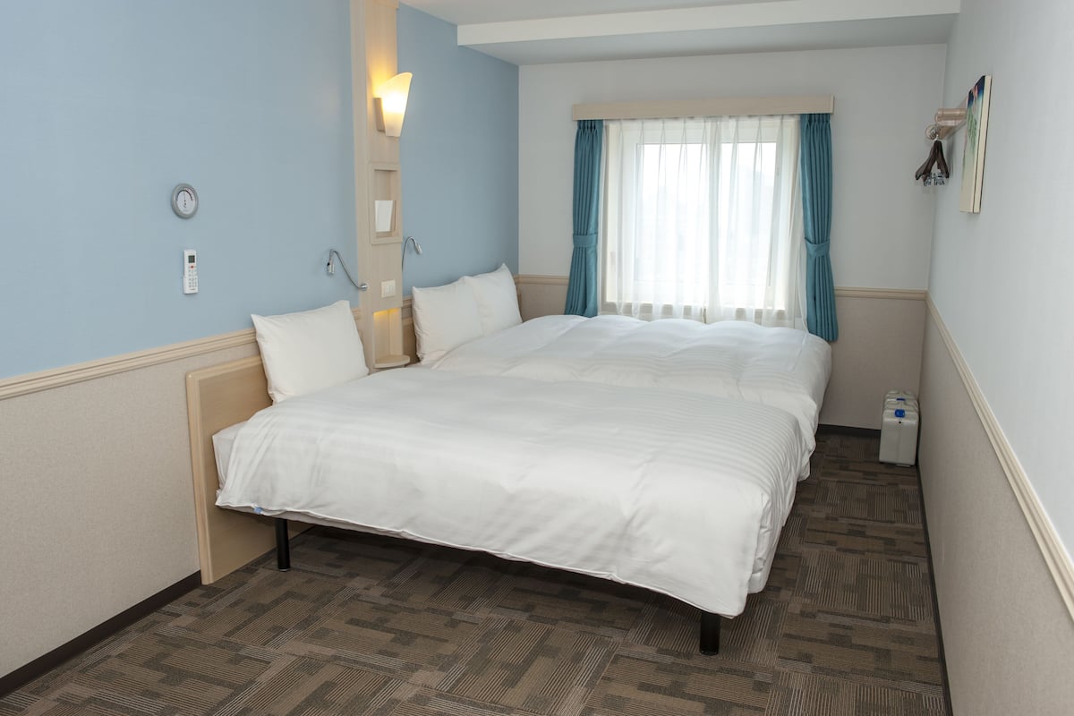 Une chambre d’hôtel avec un grand lit, une table de chevet, une horloge murale, un téléphone et une fenêtre avec des rideaux.