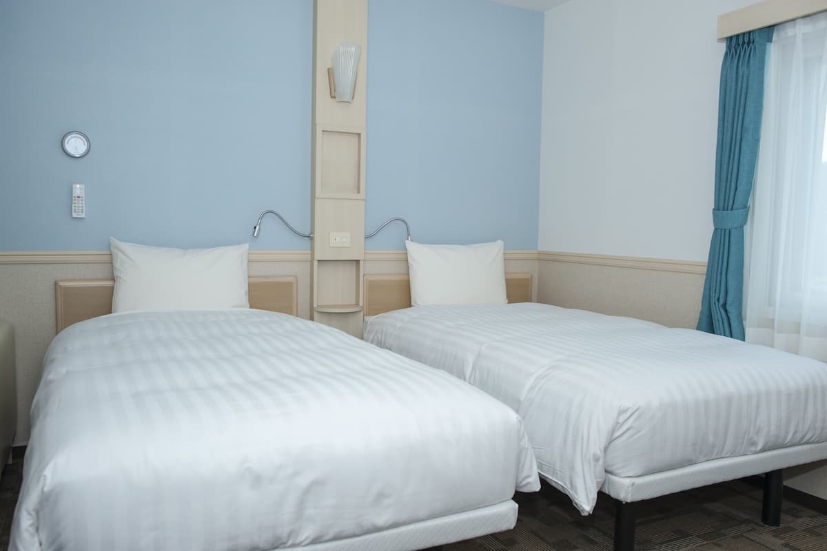 Une chambre d’hôtel avec deux lits, une table de chevet, une horloge murale et un panneau de commande fixé au mur.