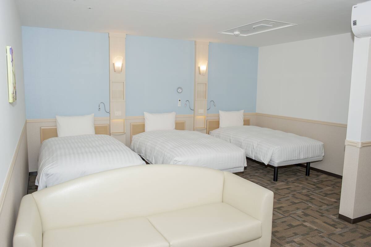 Une chambre d’hôtel avec trois lits simples, un canapé blanc et une petite table.