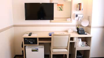 Habitación de hotel con escritorio, silla, televisión, microondas, refrigerador, cafetera y basurero.